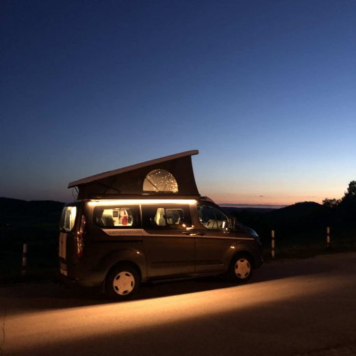 Camper mit stimmungsvoller LED-Beleuchtung, abends auf dem Berg.